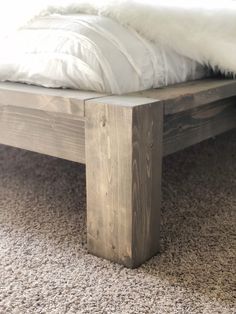 a wooden bed frame sitting on top of a carpeted floor next to a white comforter