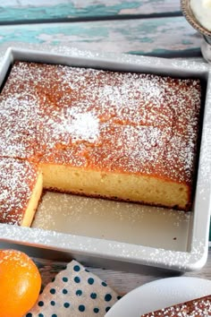 an orange cake with powdered sugar on top in a pan next to two plates