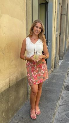 a woman standing in front of a building holding a drink and looking at the camera