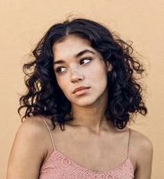 a young woman with curly hair wearing a pink tank top and looking at the camera