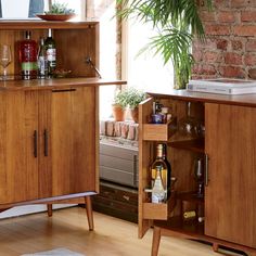 an open cabinet with liquor bottles and glasses in it next to a potted plant