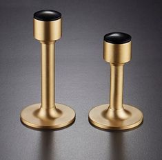 two gold and black candlesticks sitting on top of a table next to each other