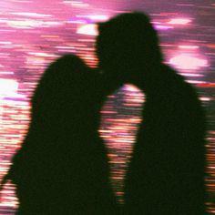 the silhouette of two people kissing in front of a cityscape at night time