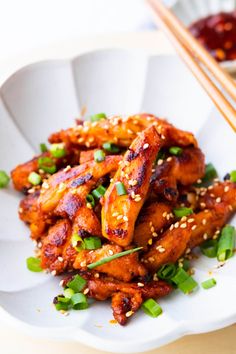 chicken with sesame seeds and green onions on a white plate next to chopsticks