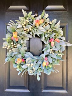 a wreath on the front door with flowers and greenery hanging from it's sides