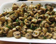 a white platter filled with mushrooms and parsley on top of a wooden table