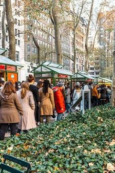 many people are walking around in the park with trees and leaves on the ground,