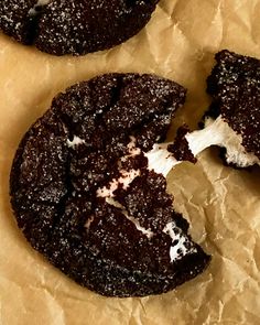 two chocolate cookies with white frosting and one half cut in half on brown paper