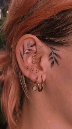 a woman with tattoos on her ear and behind the ear is a small leaf tattoo