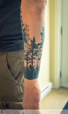 a man with a forest tattoo on his arm is standing in front of a window