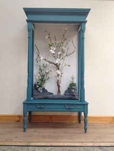 a blue cabinet with flowers and rocks in it on a wooden floor next to a wall