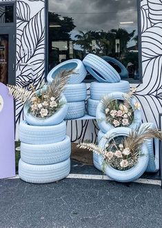 several blue tires stacked on top of each other in front of a building with plants growing out of them