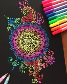 colored pencils are next to a drawing of a colorful flower on a black paper