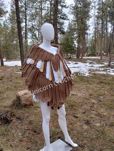 a white mannequin wearing a brown dress in the middle of a wooded area