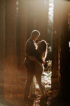 a man and woman hugging in the woods at sunset with sunlight streaming through trees behind them