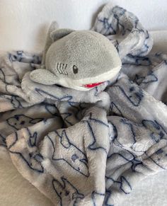 a stuffed shark wrapped in a blanket on top of a white bedding with blue writing