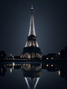 the eiffel tower lit up at night with its lights reflecting in the water