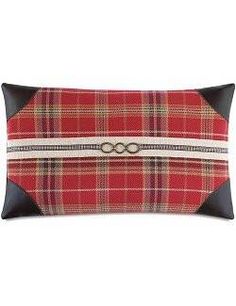 a red and black plaid pillow with an oval buckle on the front, along with leather trim