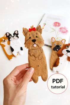 a hand holding up a small felt dog ornament in front of three other dogs