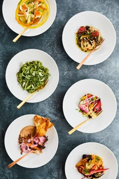 four white plates with different types of food on them and chopsticks in the middle