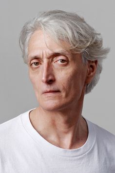 an older man with grey hair and white shirt looking at the camera while wearing a white t - shirt