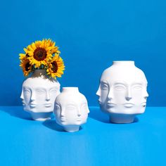 three white vases with faces and sunflower in them