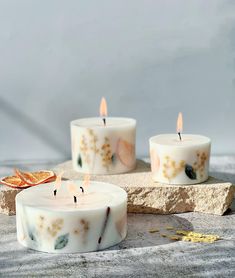 three candles sitting on top of a stone slab next to dried oranges and leaves