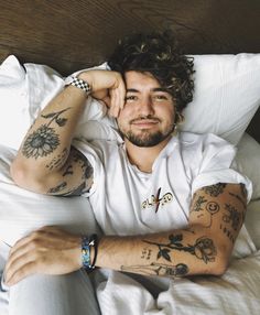 a man laying in bed with tattoos on his arms