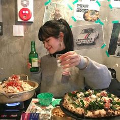 a woman sitting at a table with two pizzas and drinks in front of her