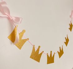 a pink and gold princess crown banner hanging from a string on a white wall with ribbon