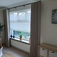 a living room with a large window covered in curtains and potted plants on the windowsill