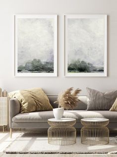 two paintings hang on the wall above a couch in a living room with white walls