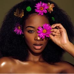 a woman with flowers in her hair is holding two pink flowers up to her face