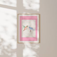 two birds are flying in the air near a pink and white framed artwork on a wall