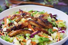 a white bowl filled with chicken, lettuce and carrots on top of a table