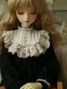 a doll sitting on top of a wooden chair wearing a black dress with white ruffles