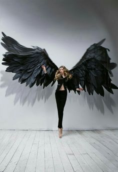 a woman with black wings on her body posing for a photo in front of a white wall