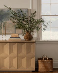 a plant in a vase sitting on top of a wooden cabinet next to a window