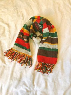 a multicolored striped scarf laying on top of a bed next to a white pillow