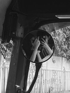 a woman is looking at her reflection in the side mirror of a car as she holds her hands up