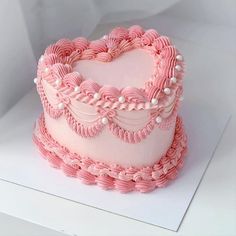 a heart shaped cake with pink icing and pearls on it's edges, sitting on a white surface