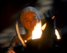 a woman with white hair and piercings sitting in front of a fire lit candle