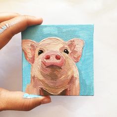 a hand holding up a small painting of a pig