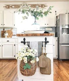 a kitchen with white cabinets and flowers in a basket on the island, along with cutting board utensils