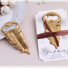 the golden feather key chain is next to a white plate with flowers and a brown ribbon