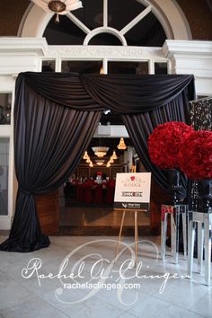 the entrance to an event with black drapes and red flowers in vases on display