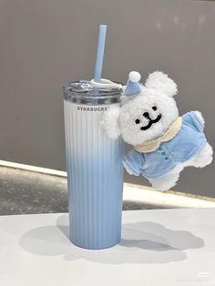 a white teddy bear sitting next to a blue cup with a straw in it's mouth