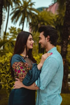 a man and woman standing next to each other in front of palm trees with their arms around each other