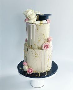 a three tiered cake with flowers and graduation cap on top, sitting on a pedestal