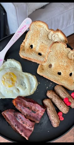 a black plate topped with toast, bacon and eggs next to two slices of bread